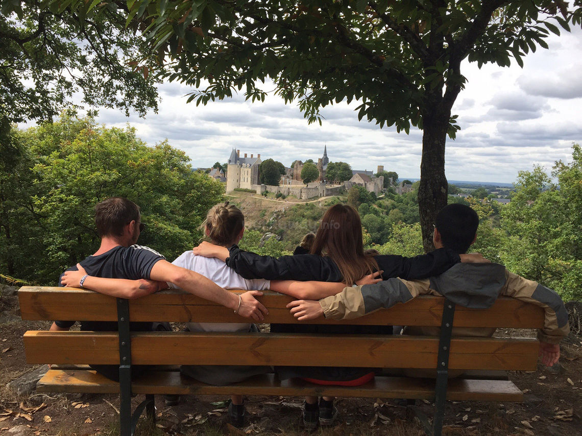 four travellers sitting on bench arms around each others backs and enjoying castle view from above