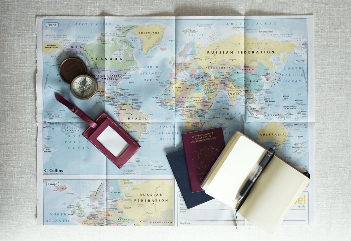 world map with passport, notebook and compass on top