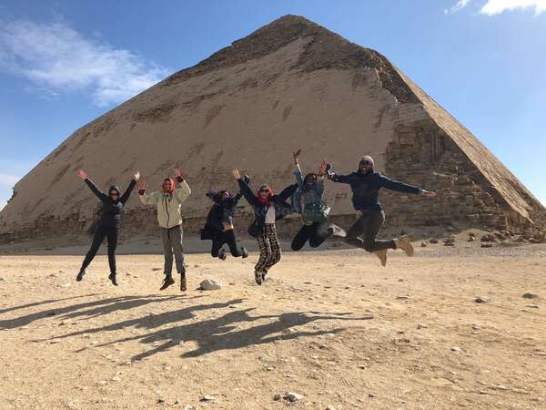 travellers friends jump and pose in front of a pyramid Egypt adventure