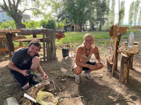 pair of male and female workawayers smiling while stringing shells together outdoors eco building decoration project