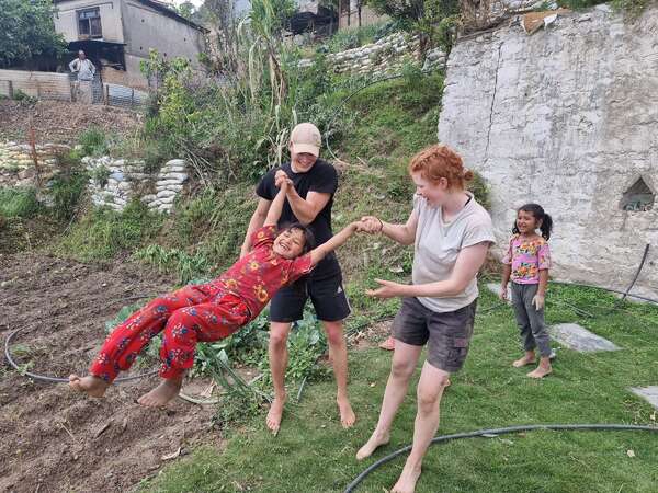 two smiling female travellers swinging a young girl while another laughs at the back in the garden