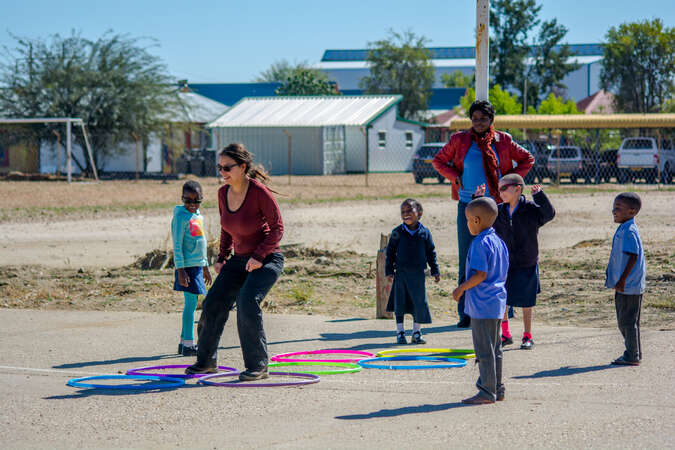 workawayer expat playing hopscotch with smiling children in uniforms while teacher looks on