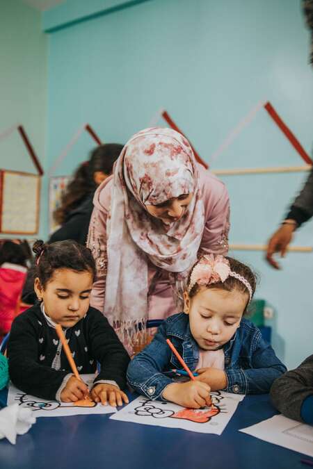 smiling teacher looking down at two students colouring hello kitty