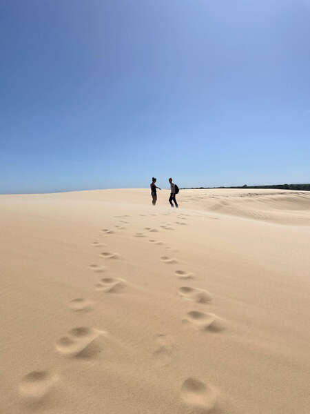 two travellers hiking up a sand dune