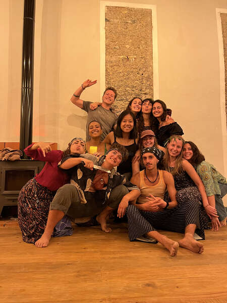 A group of twelve young people indoors, huddled closely in a group for the shot. They are all smiling and look excited! Some of them are in fancy dresses with accessories like bandanas, drawn-on tattoos and fake swords.