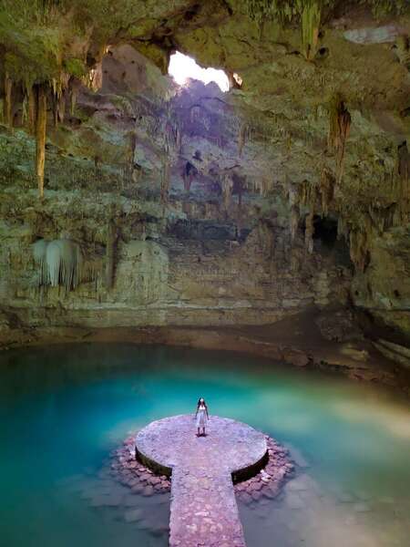 solo travel woman standing in cenote gazing up light cave explore Mexico