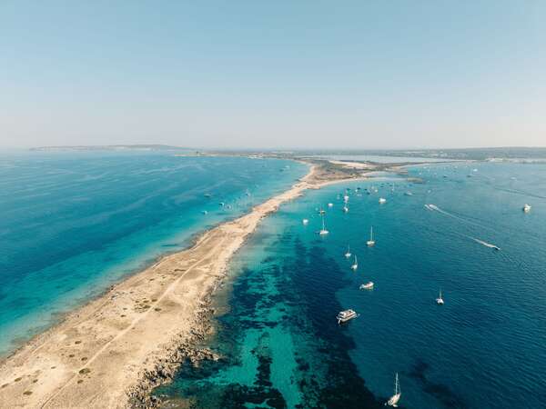 Aerial view of a coastline with turquoise waters, white sand and sailing boats in Formentera, Balearic Islands.