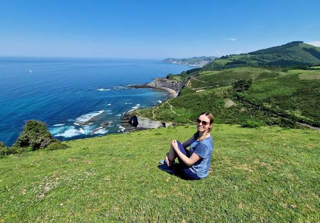 Angelina, blog post author, sits on the grass with the ocean in the background in the Basque Country, near Ondarroa.
