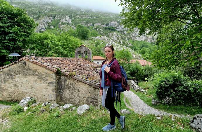 Angelina, blog post author, stands in front of traditional stone church with the mountains in the background in Picos de Europa, Asturias.