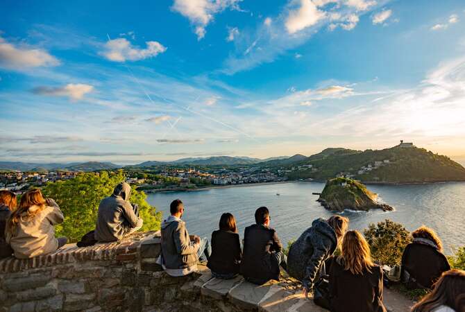 A group of young people sitting together on the rocks, viewing the city of San Sebastian (Donostia) in the Basque Country.