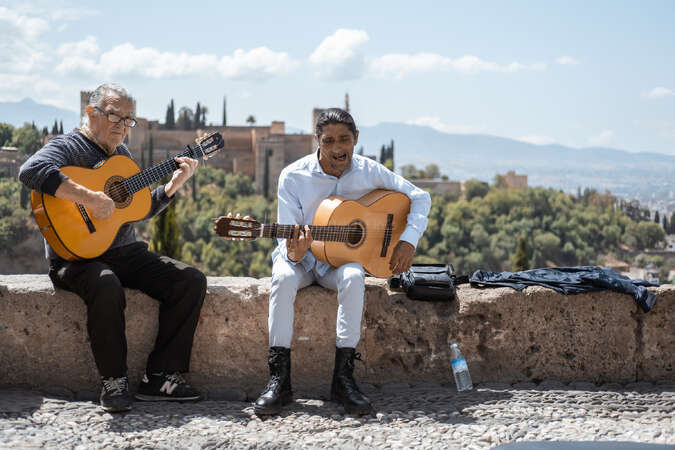 Two musicians playing guitars on the hill in Granada, Spain, with Alhambra complex in the background.