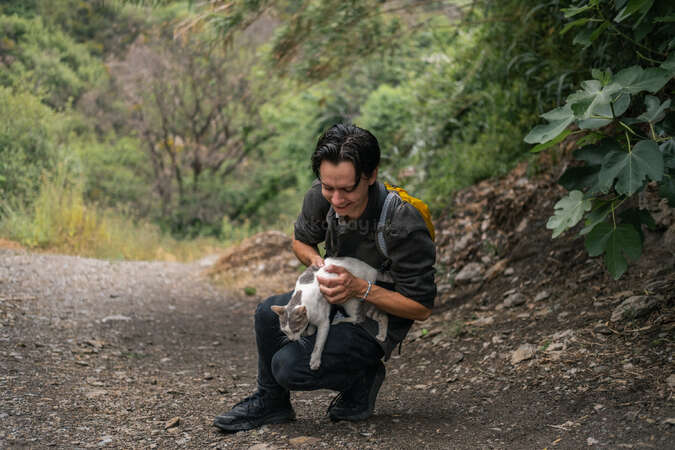 best-places-spain-house-sitting-sierra-nevada-workaway-gallery Man holding a cat while hiking on a forest trail in Sierra Nevada, Spain.